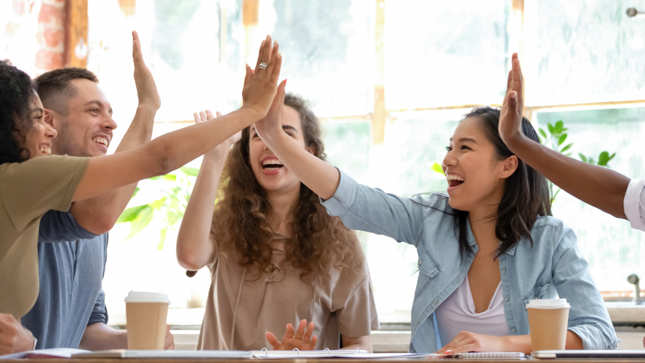 Group of people high-fiving over a table with coffee cups.