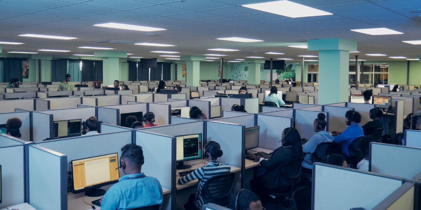 A large room with cubicles and a person is seated in each one, looking at a screen and wearing a headset.