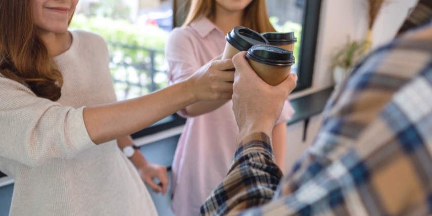 A group of people stand facing one another, clinking their to-go coffee cups in a "cheers."